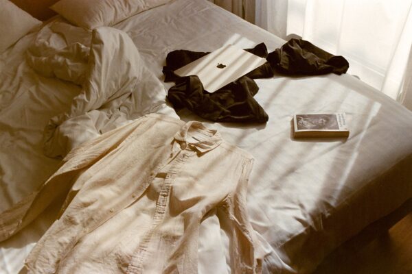 A relaxed bedroom scene featuring clothes, a book, and a tablet on a bed