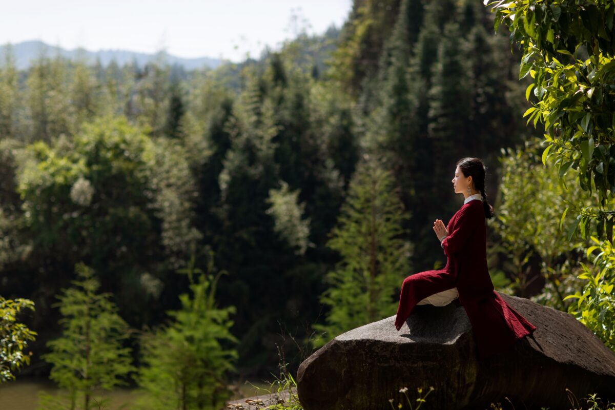 Asian woman in traditional clothing meditating on a rock in a serene forest setting