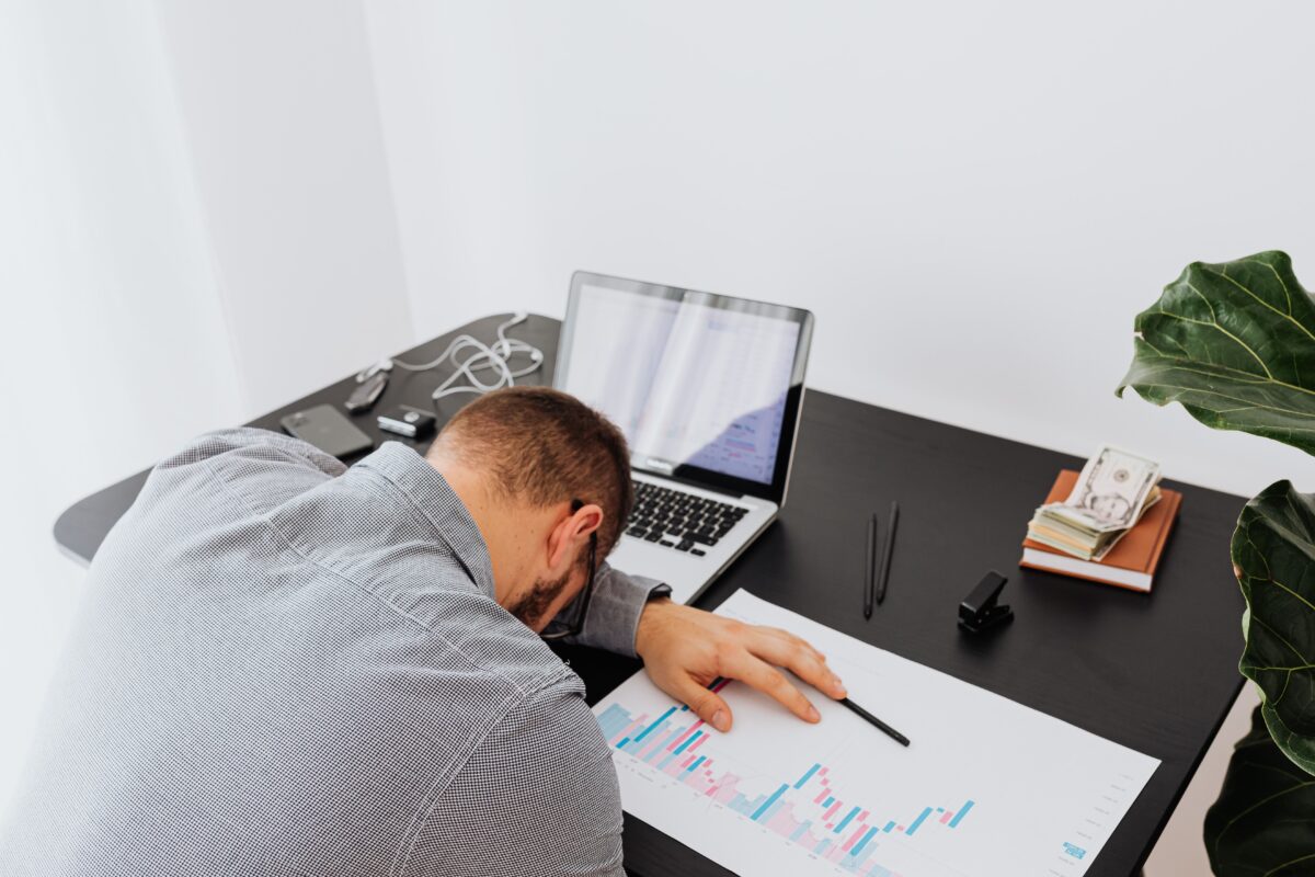 Overworked businessman falling asleep on office desk with laptop and charts