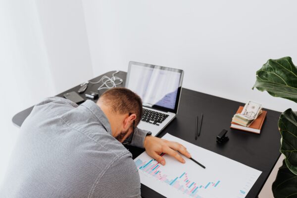 Overworked businessman falling asleep on office desk with laptop and charts
