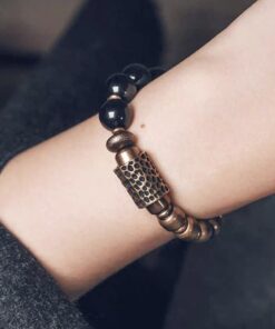 Close wrist view of the textured brass tube and black obsidian beads