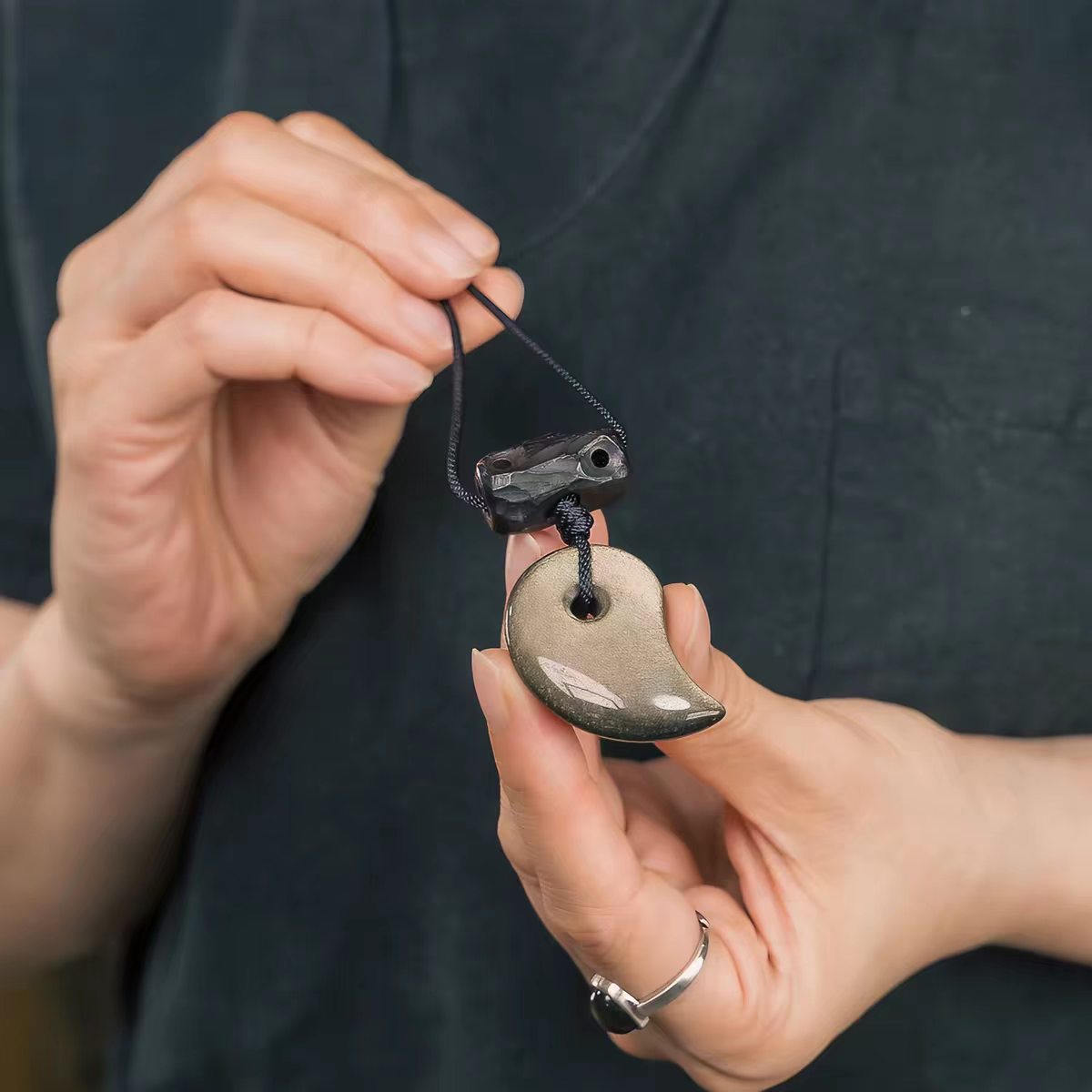 Xuan Yao gold sheen obsidian half-moon pendant held in hands to show its approximate size