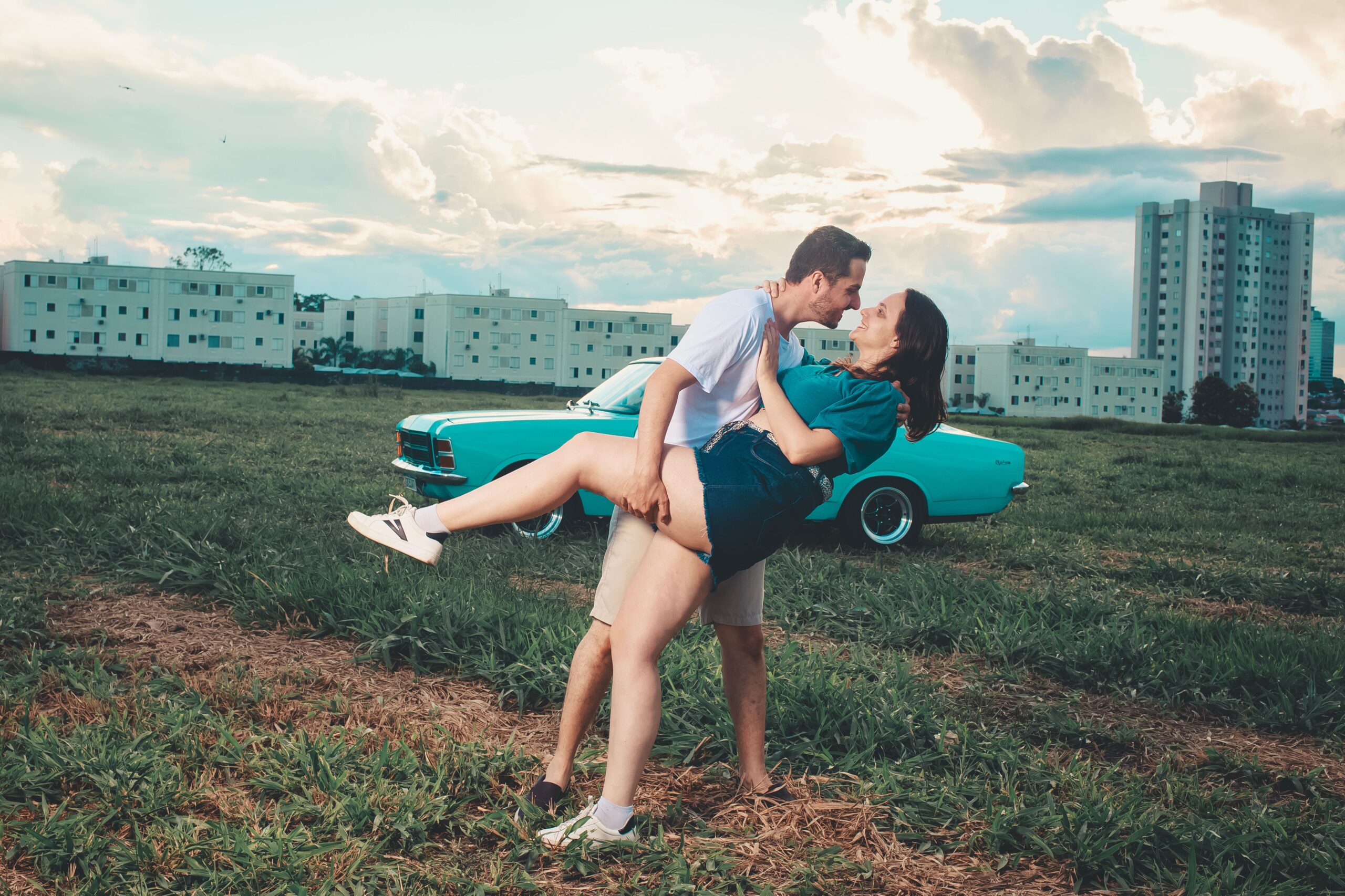 Couple embracing in an open field beside a parked car