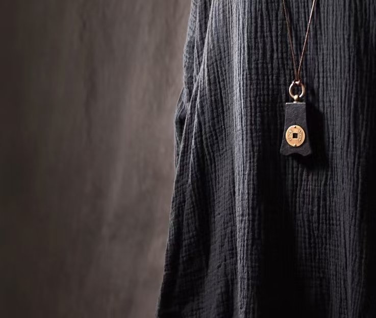 Bao Pu Qian (Embracing Simplicity Coin) Pendant — coin-motif pendant necklace worn over dark fabric