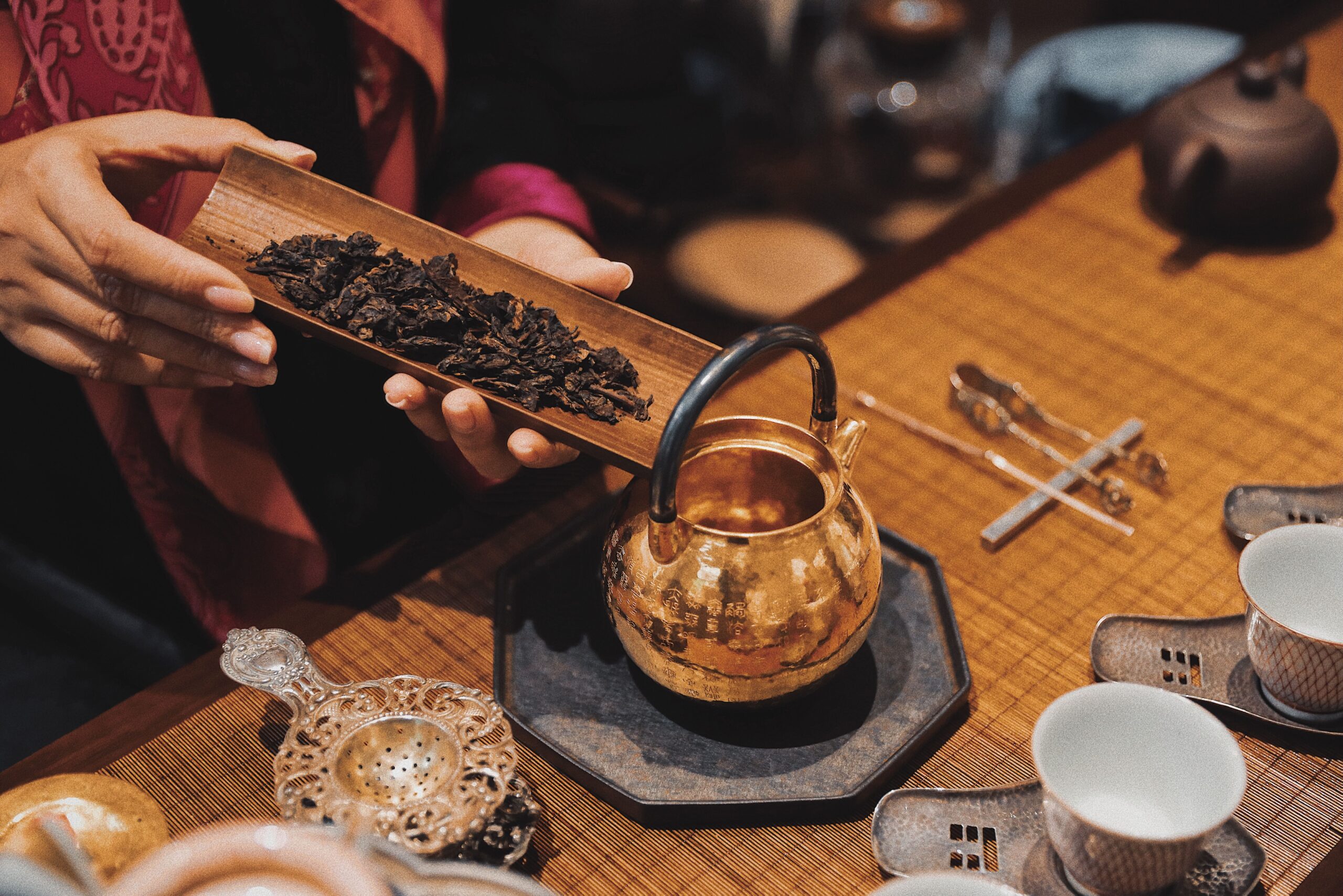 Hands preparing tea beside a gold-colored kettle