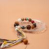 Bodhi Seed, Sandalwood & Dzi Bead Bracelet — multicolored bead bracelet with tassels on a clear dish