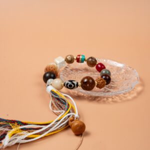 Bodhi Seed, Sandalwood & Dzi Bead Bracelet — multicolored bead bracelet with tassels on a clear dish