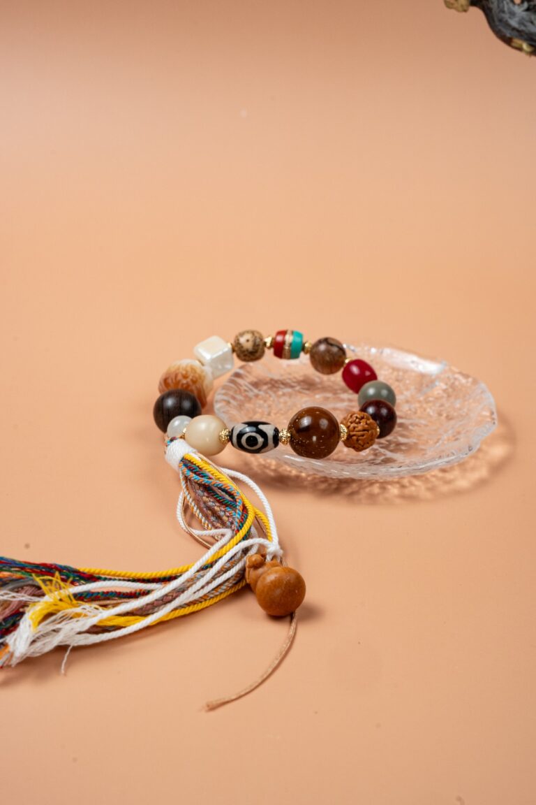 Bodhi Seed, Sandalwood & Dzi Bead Bracelet — multicolored bead bracelet with tassels on a clear dish