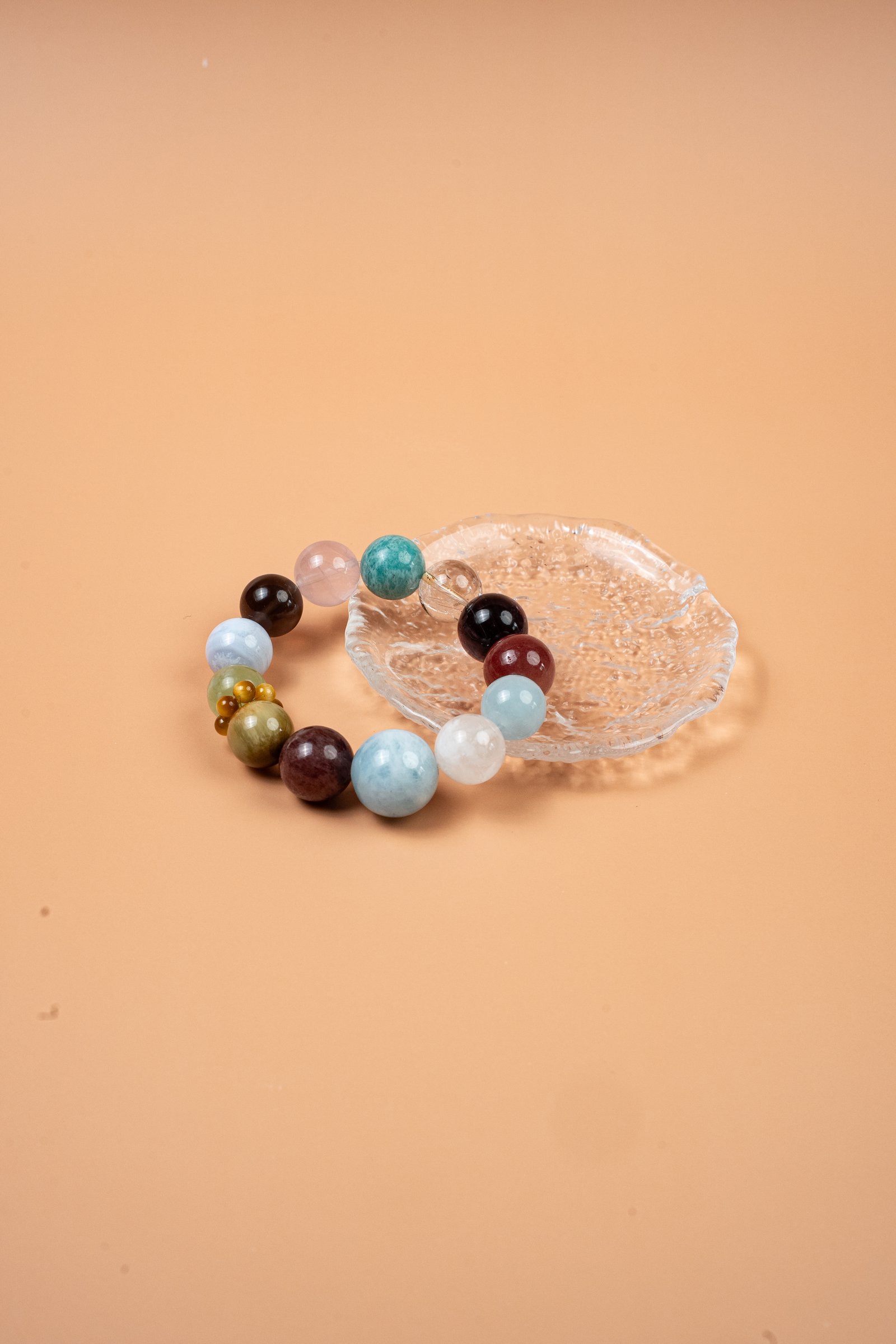 Earth Multi-Gemstone Aquamarine Golden Tiger Bracelet — multicolored translucent bead bracelet on a clear dish