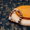 Feizi Xiao Goose Pear Herbal Incense Bracelet — brown bead bracelet with pale accents on a wooden display