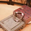 Feizi Xiao Goose Pear Herbal Incense Bracelet — brown bead bracelet with pale accents beside a patterned box