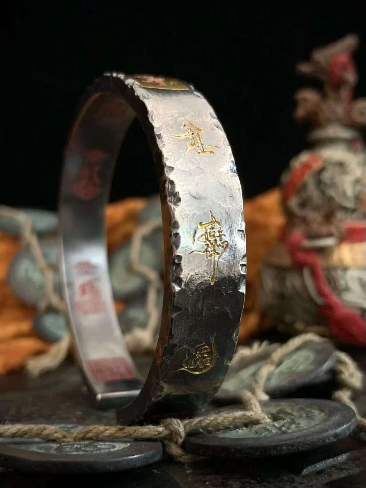 Open cuff bracelet with engraved gold-colored symbols, displayed beside coins