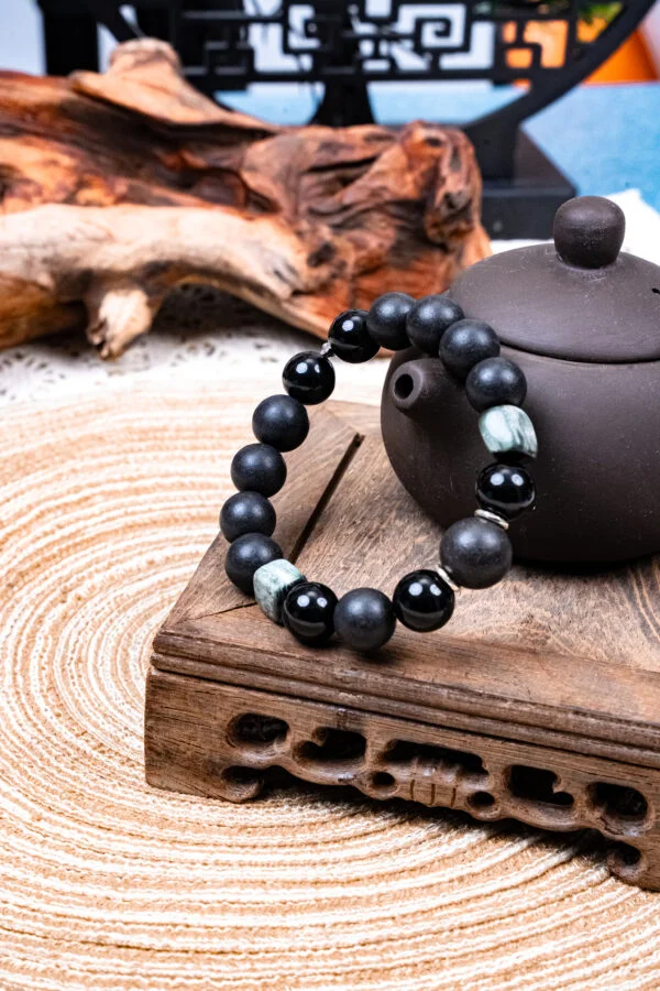 Heilong Xian Herbal Incense Obsidian Bracelet — dark bead bracelet with metallic accents beside a teapot