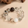 Ink-Wash Phantom Quartz Bracelet — translucent bead bracelet with dark inclusions beside wood