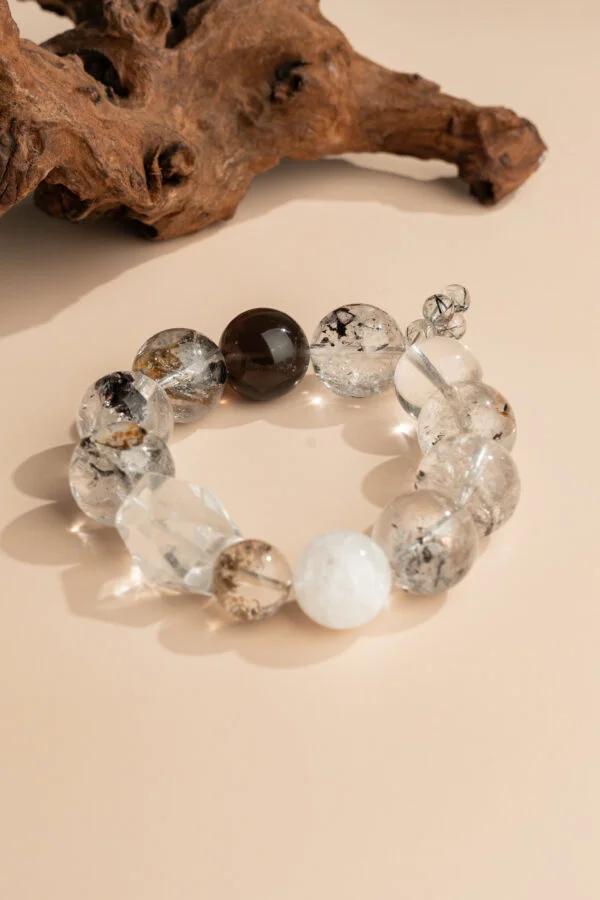 Ink-Wash Phantom Quartz Bracelet — translucent bead bracelet with dark inclusions beside wood