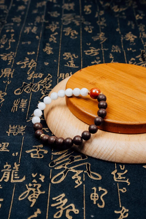 Jiang Zhen Xiang Herbal Incense Bracelet — white and brown bead bracelet on a wooden display