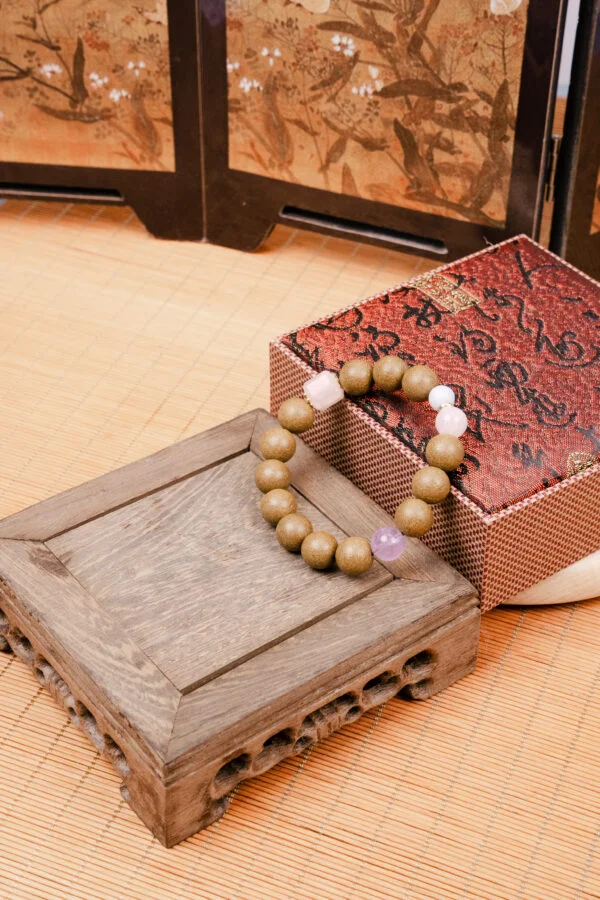 Muxi Xiang Herbal Incense Bracelet — brown bead bracelet with pale accents beside a patterned box