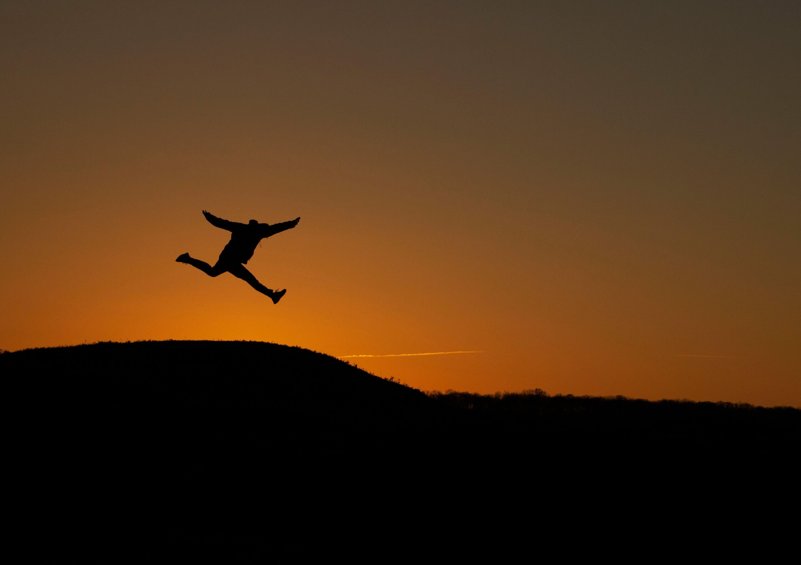 Person leaping above a hill at sunset