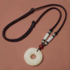 Pixiu Jade Pendant — pale circular pendant with its long cord on a plain surface