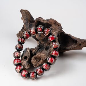 Red Incense Ash Liuli Bead Bracelet — red and black patterned bead bracelet propped against wood