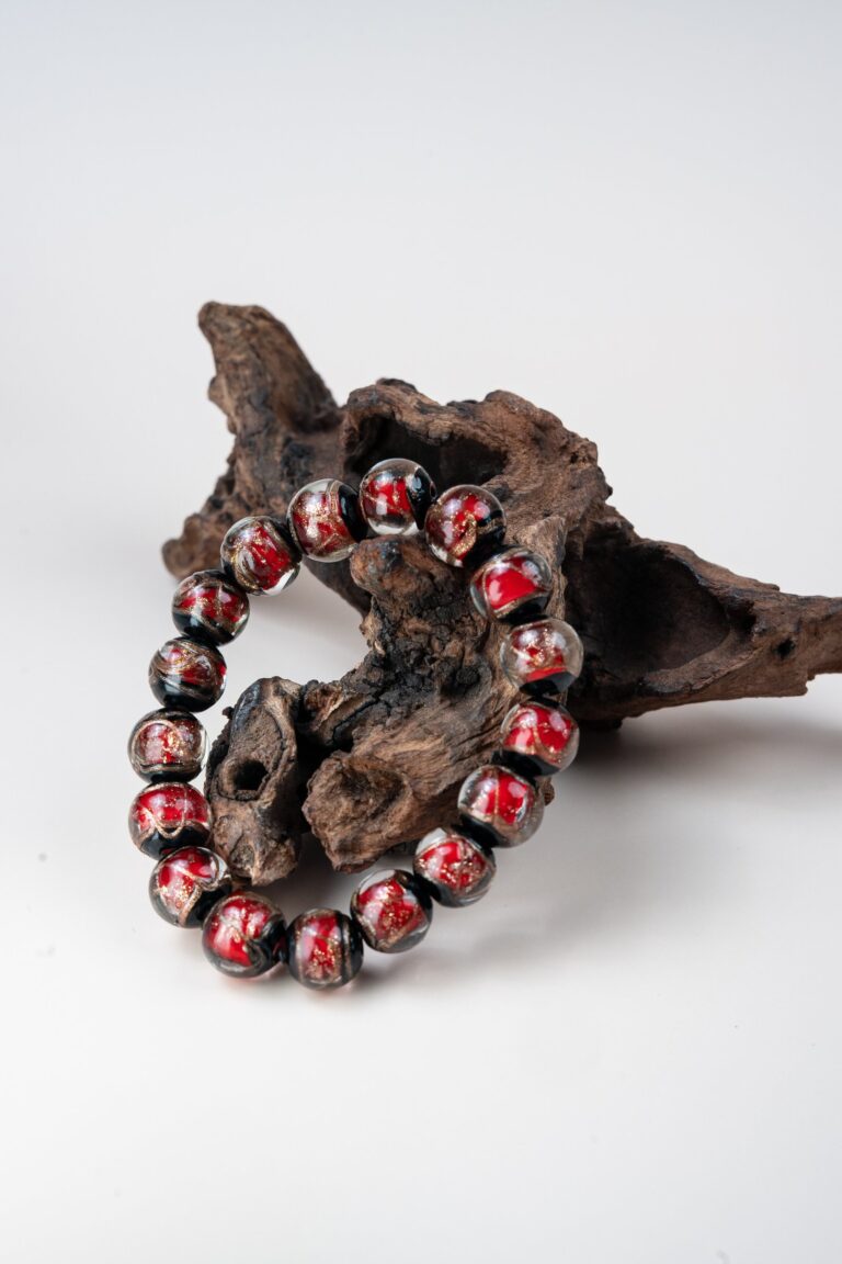 Red Incense Ash Liuli Bead Bracelet — red and black patterned bead bracelet propped against wood
