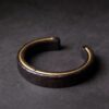 The Silent One Ebony Wood Bracelet — dark open cuff resting on a textured surface