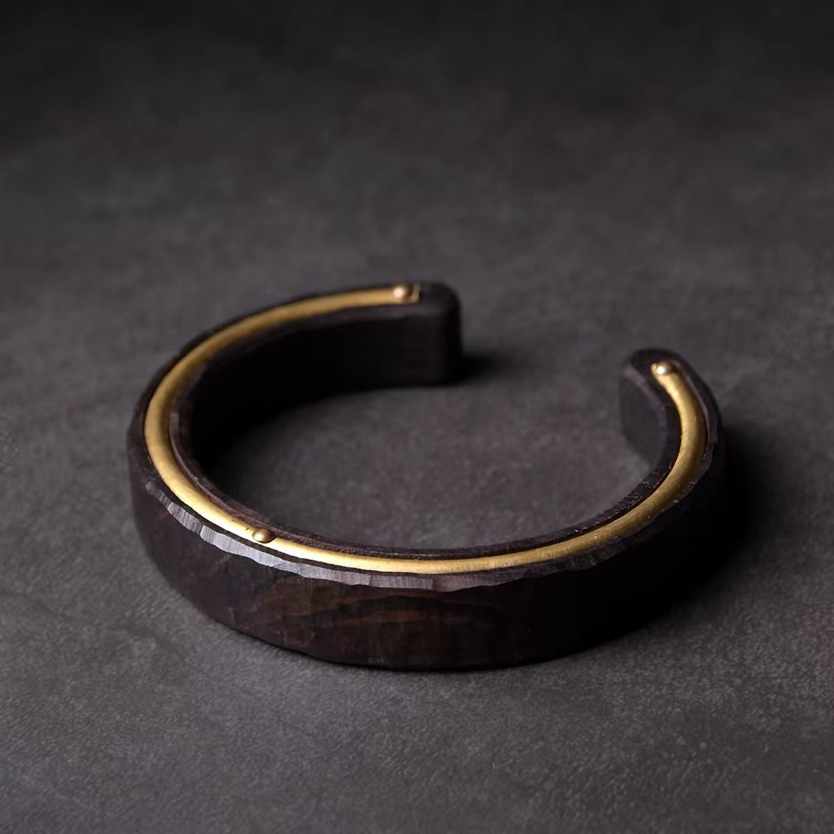 The Silent One Ebony Wood Bracelet — dark open cuff resting on a textured surface