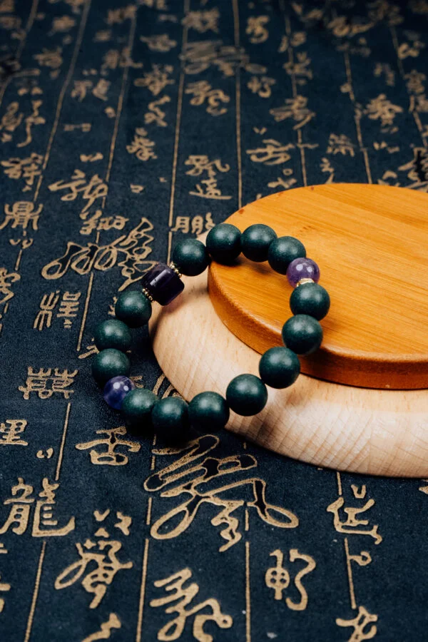 Zhizi Hexiang Herbal Incense Bracelet — dark green bead bracelet with purple accents on a wooden display